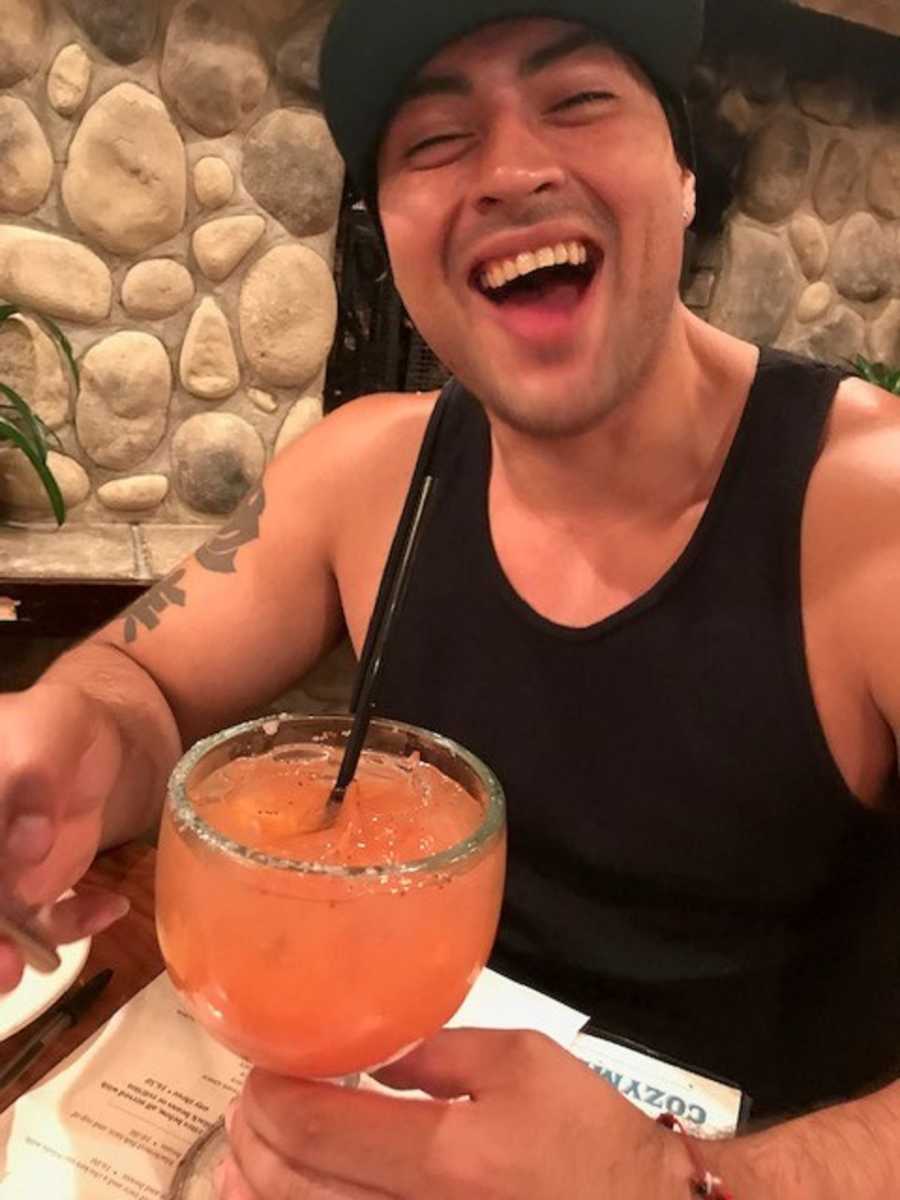 Man who has since passed from heroin addiction smiles at restaurant table with large margarita
