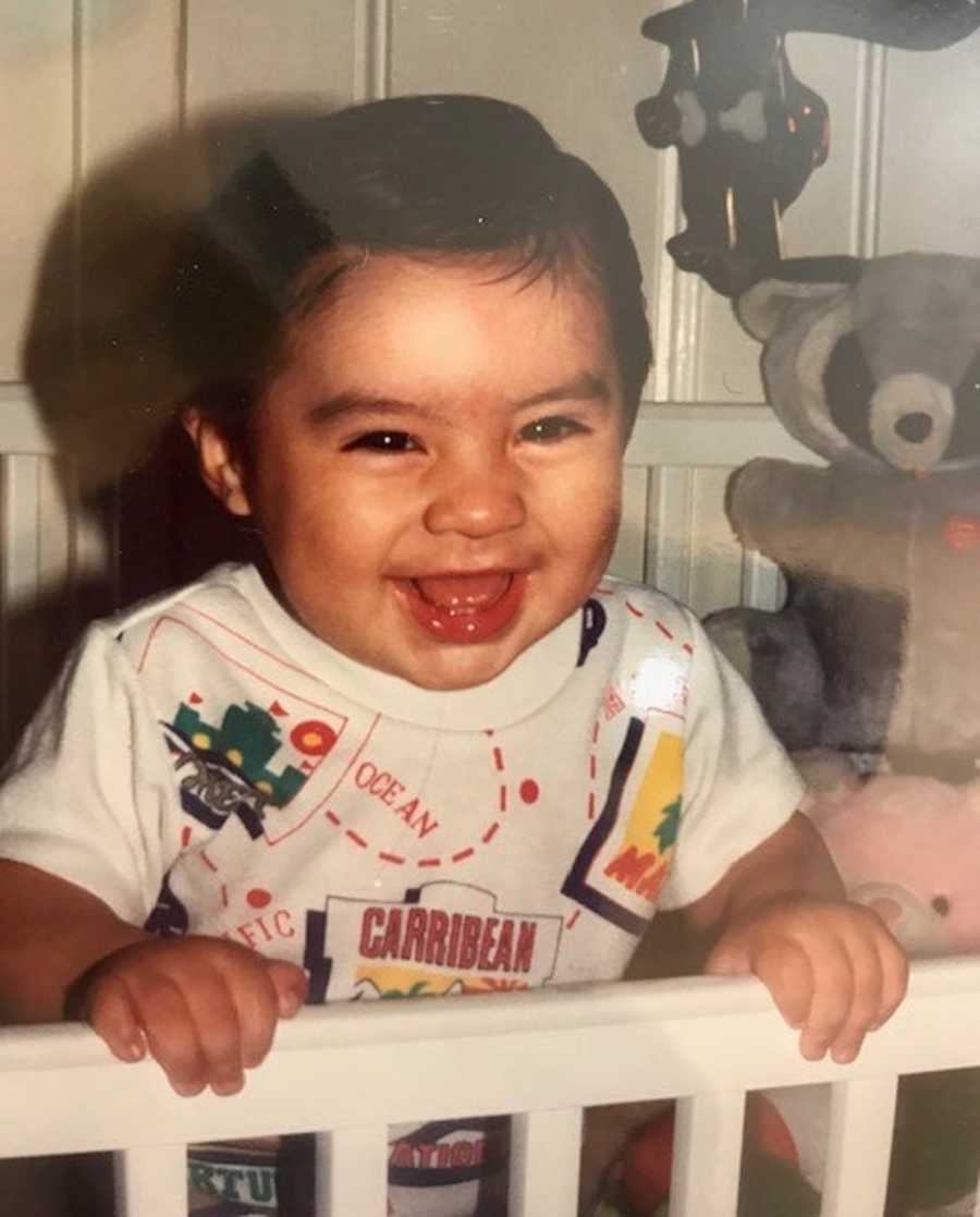 Baby standing and smiling in crib who will later in life die from heroin addiction