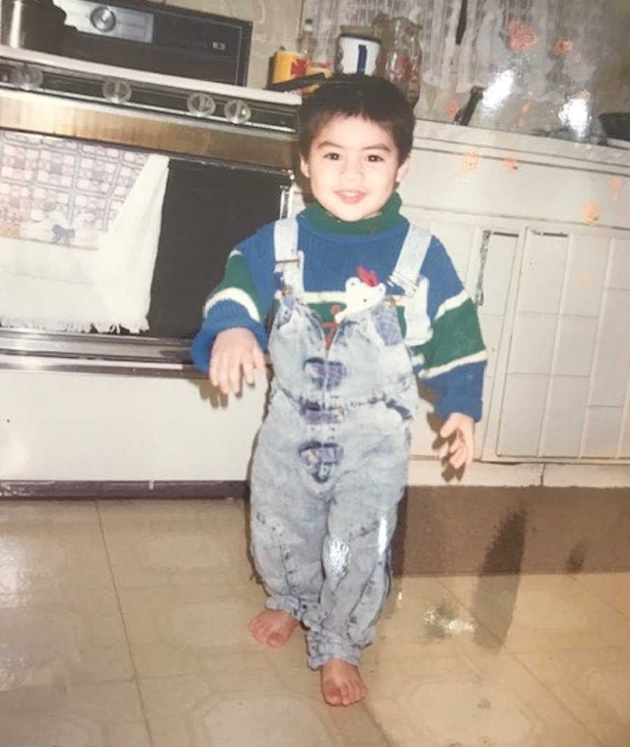 Toddler stands in kitchen in jean overalls and will later in life die from heroin addiction