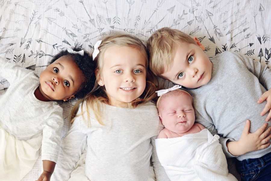 Adopted baby lays on her back beside three biological children