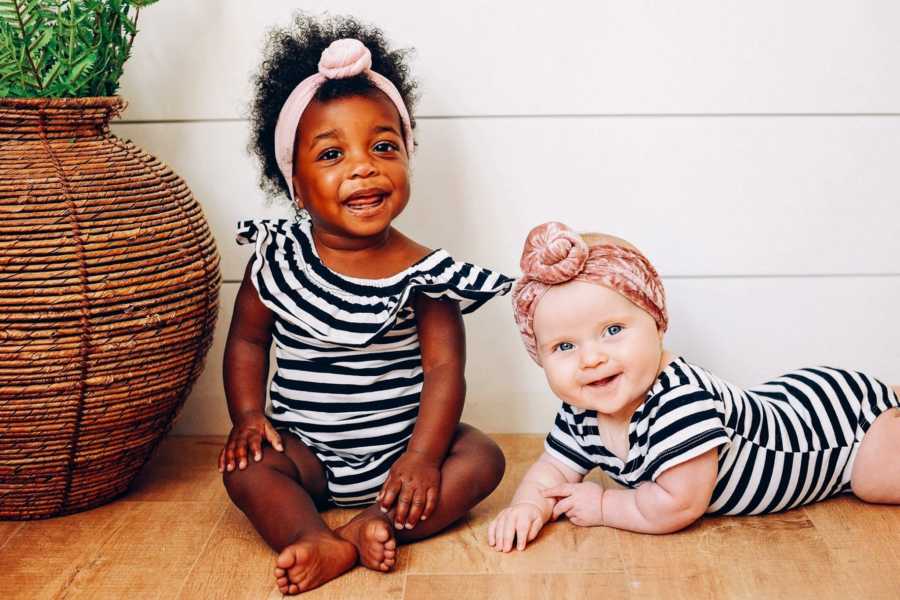Woman's adopted baby and biological baby sit on floor in matching black and white stripe onesie