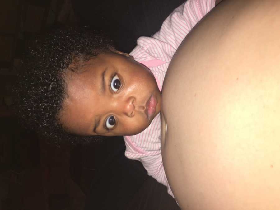 African American baby stares with wide eyes at adopted mother's pregnant stomach