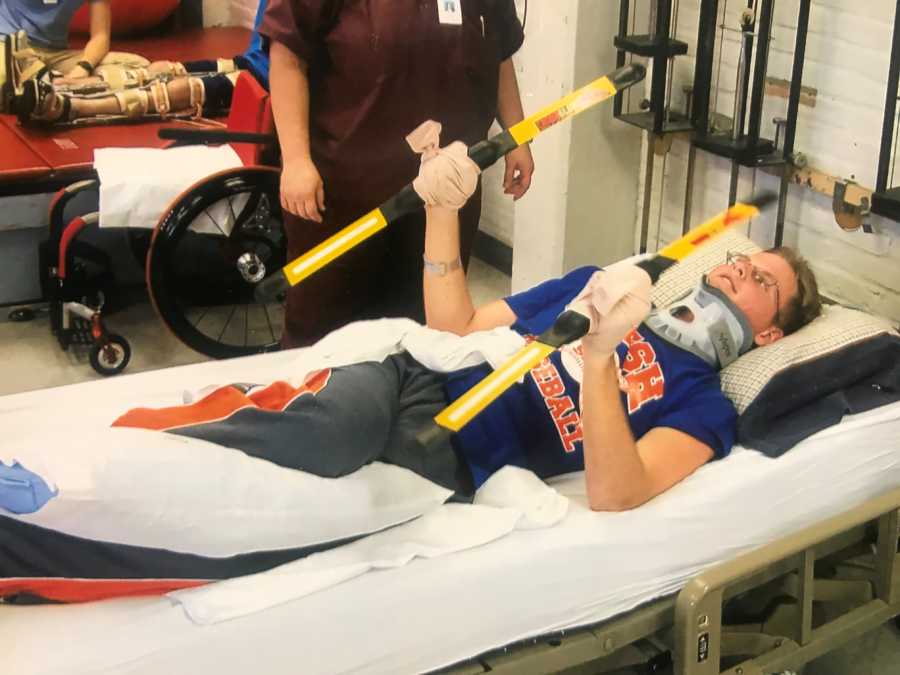 High school teen who was in car crash lays in physical therapy in neck brace holding two poles
