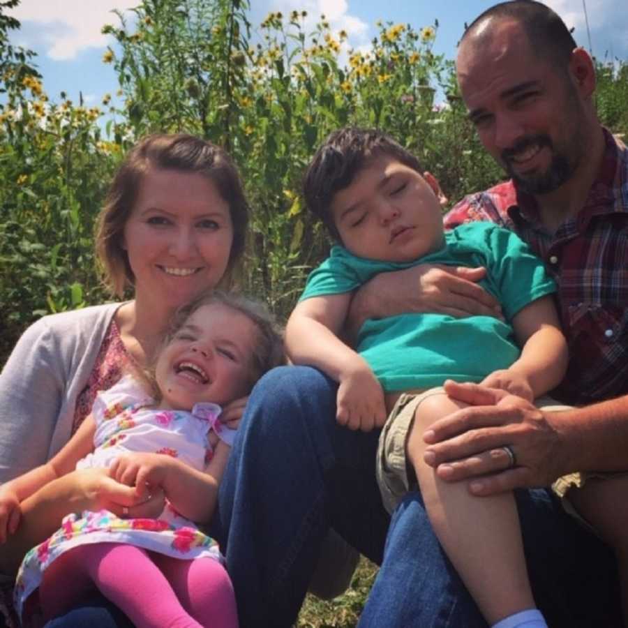 Husband and wife sit in sunflower field with two foster children with shaken child syndrome