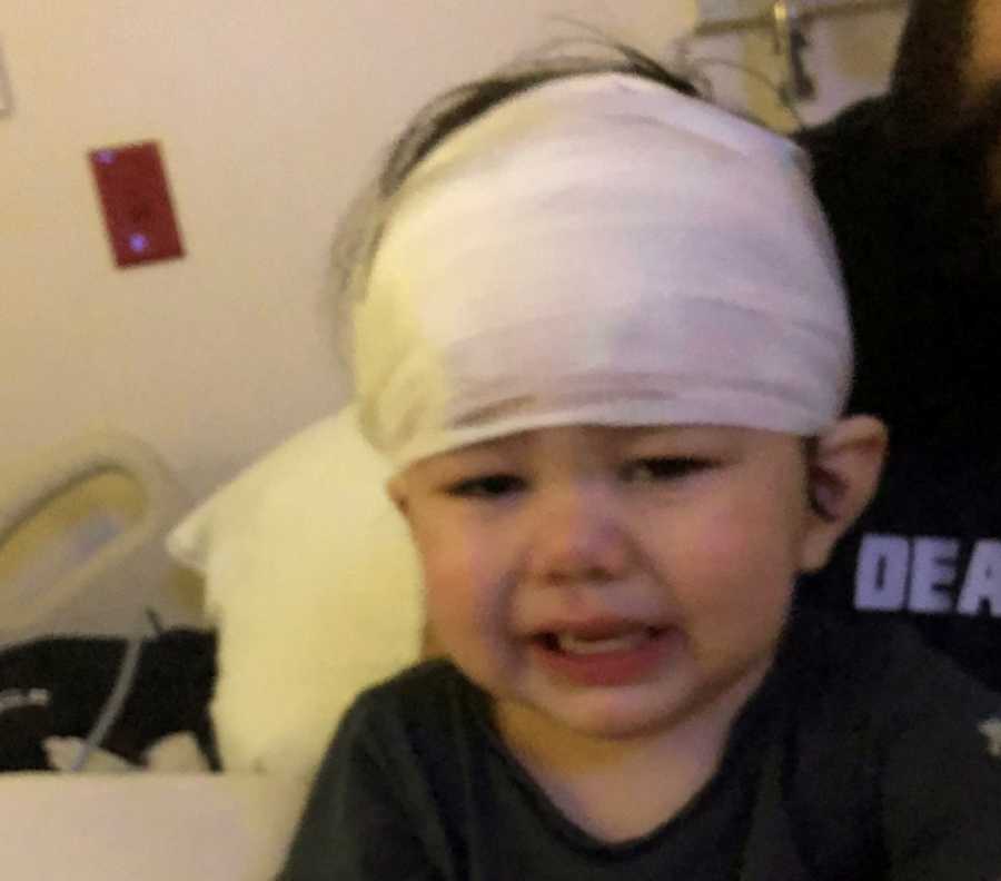 Little boy who had seizure sits in hospital room crying with bandages wrapped around his head