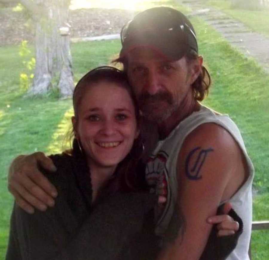 Young woman smiles as her dad wraps his arms around her