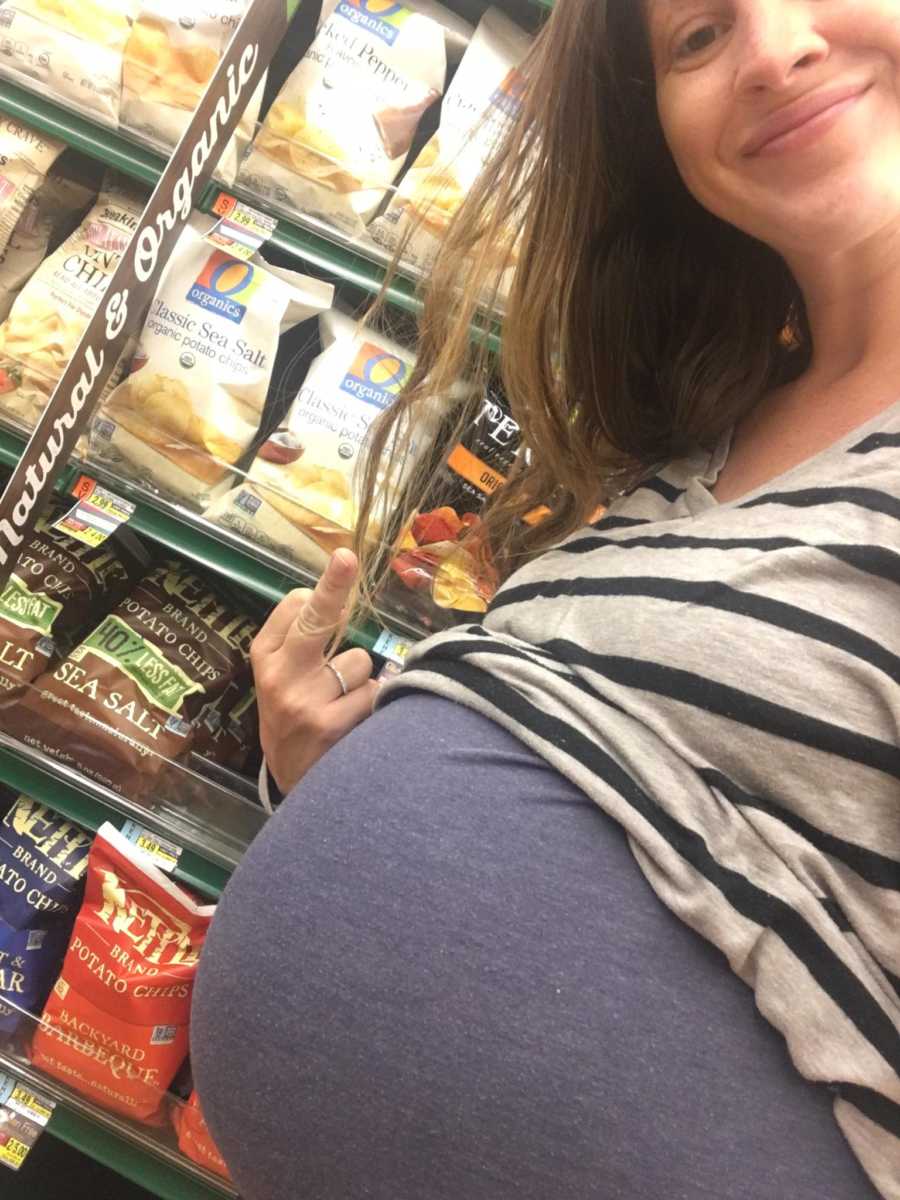 Pregnant woman stands smiling in selfie in grocery store aisle with raised middle finger