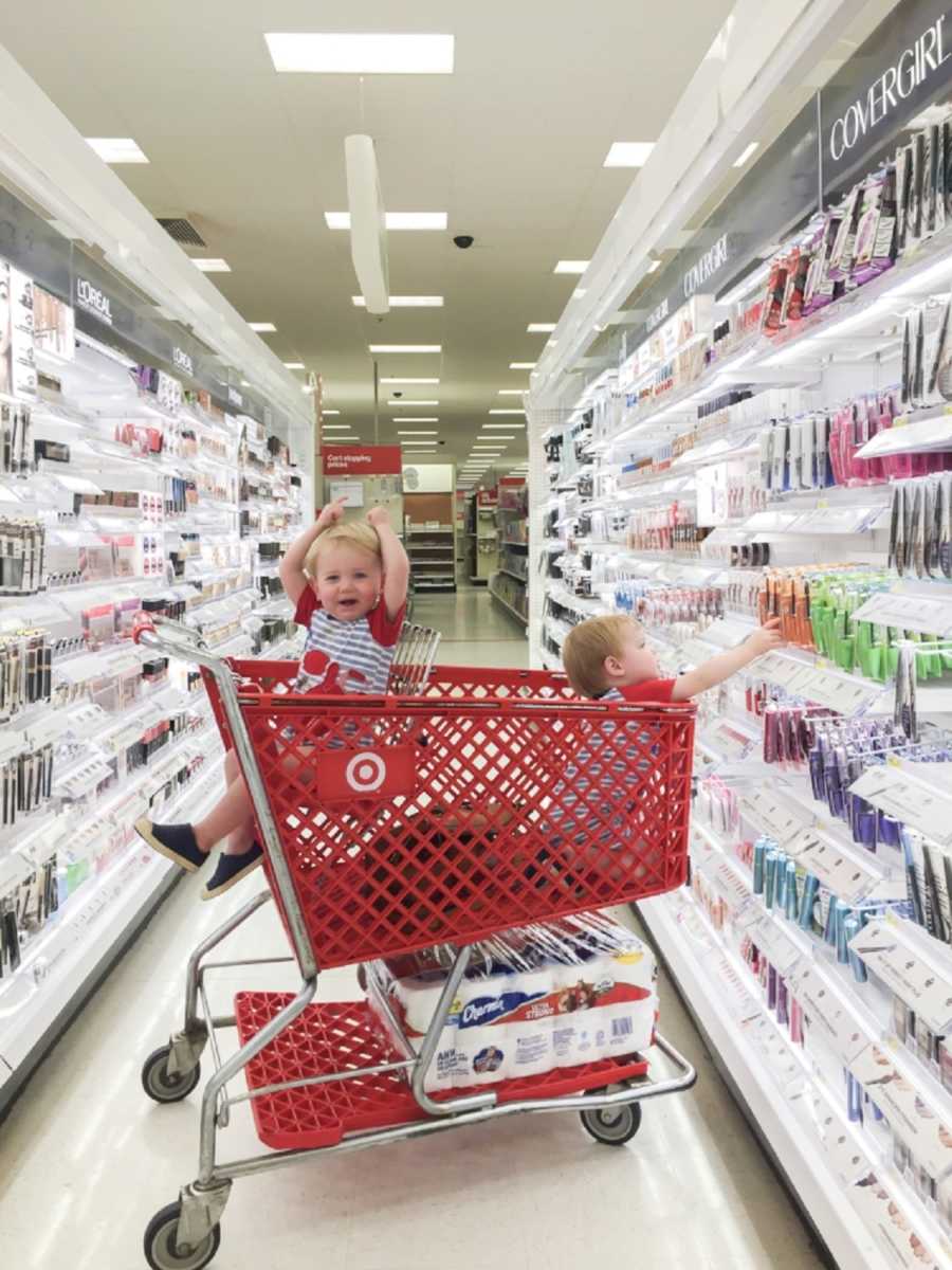 Toddlers sitting in Target shopping cart reaching for makeup in aisle of Target
