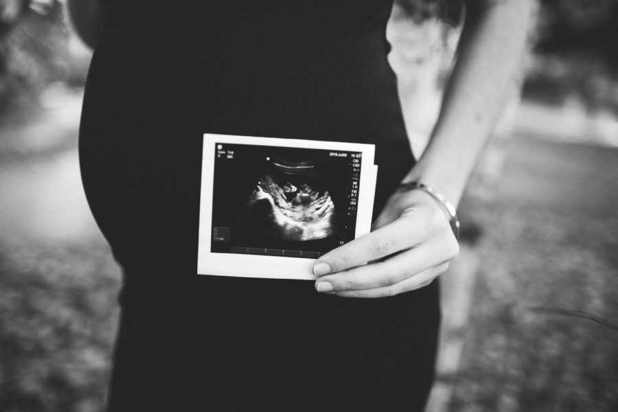 Pregnant woman holding ultrasound picture beside her stomach