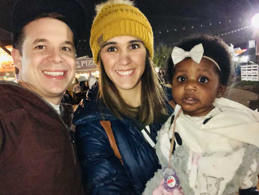 Husband and wife stand outside at night with their adopted baby girl 