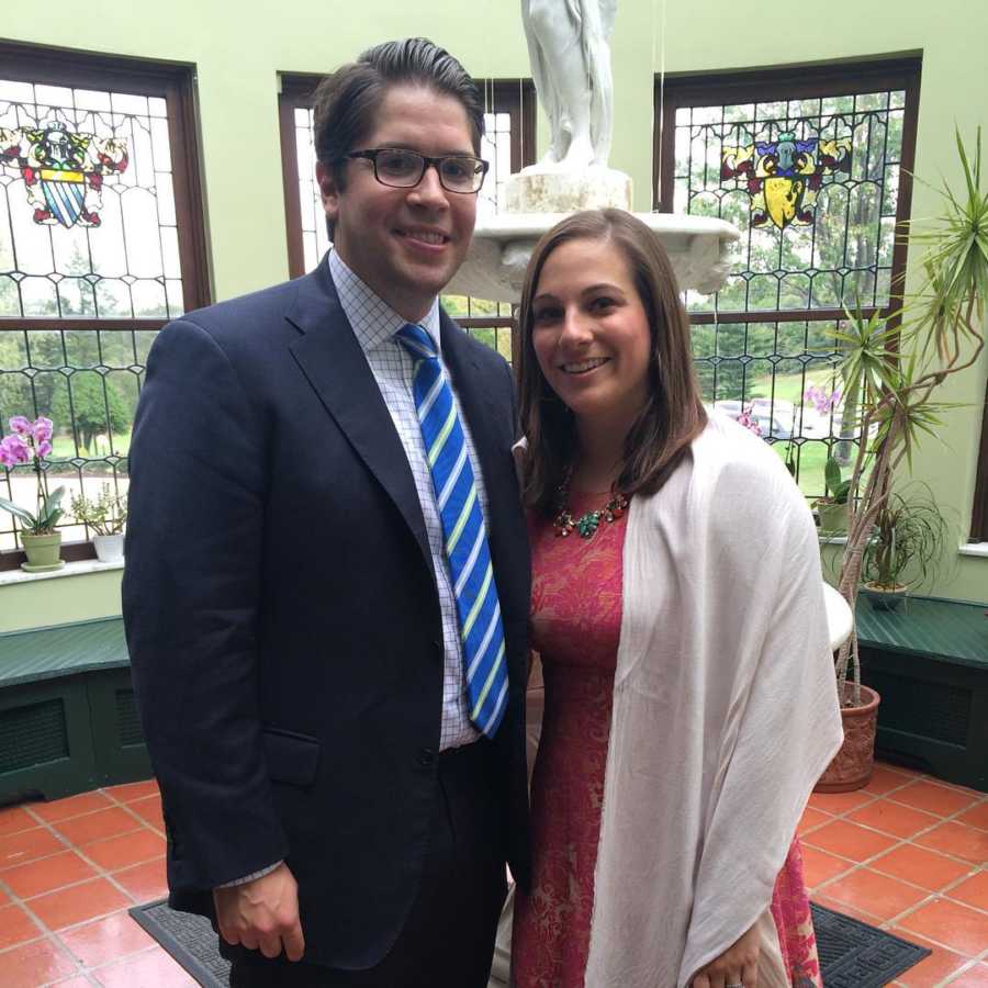 Husband and wife who are expecting triplets stand arm in arm in nice clothing