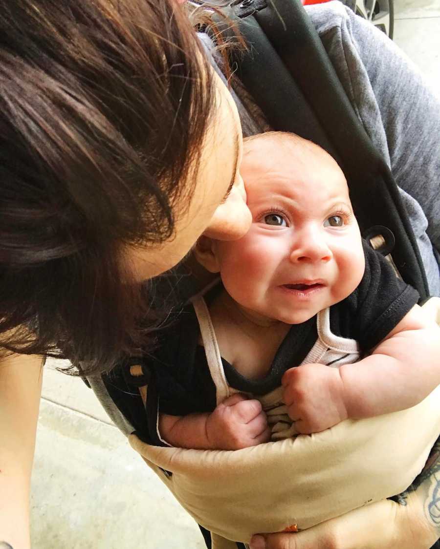 Mother kisses head of baby with Lissencephaly that is swaddled to her chest