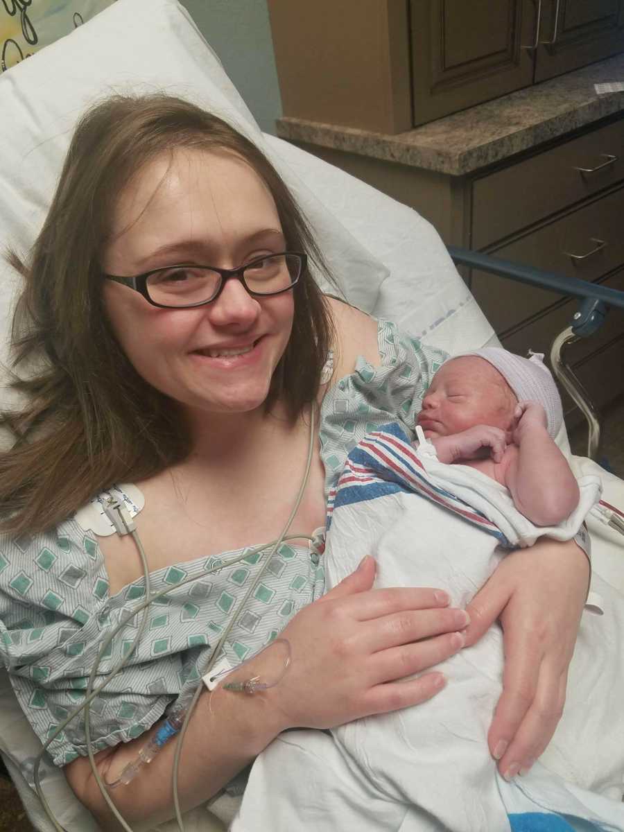 Woman with endometriosis lays smiling in hospital bed holding newborn 