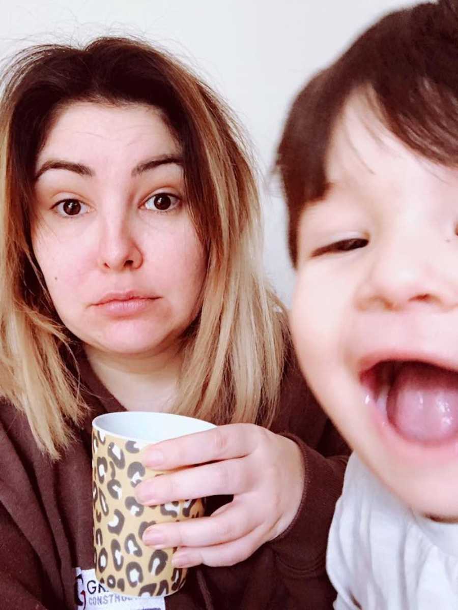 Mother who is kept up all night by toddler son takes selfie holding cheetah print mug with son whose mouth is wide open