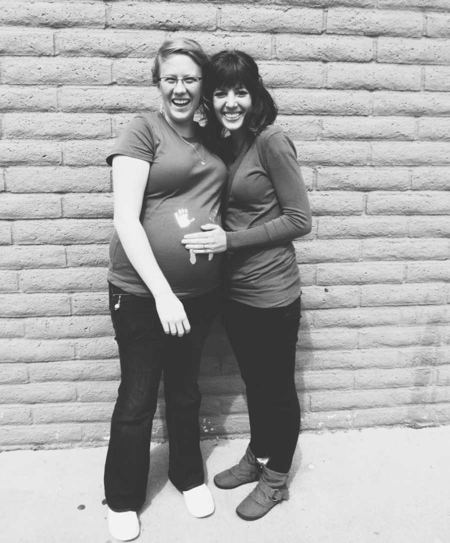 Woman stands beside pregnant woman who is carrying the baby she will adopt in front of brick wall
