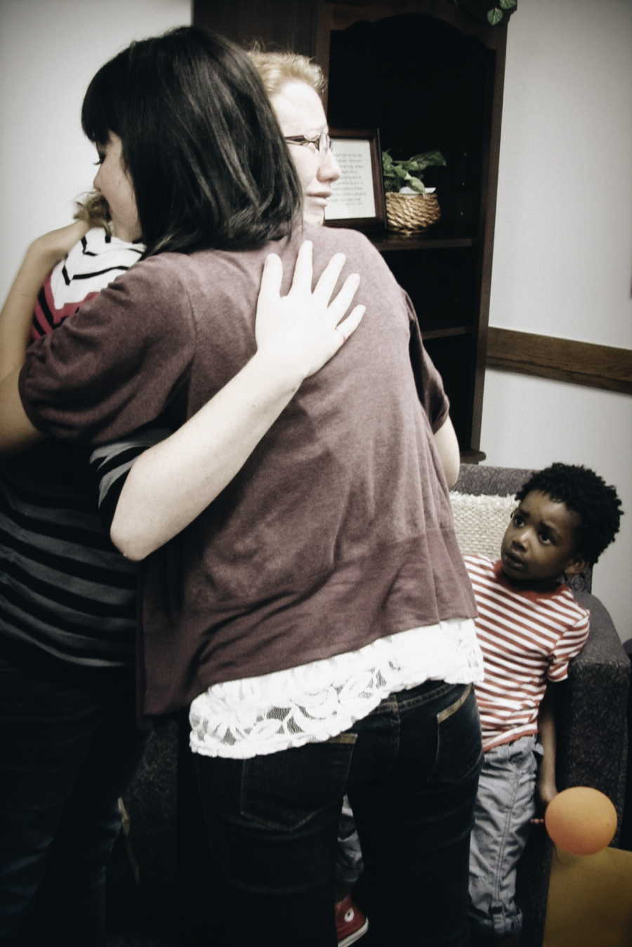 Mother hugs woman who had the baby she is adopting with her other adopted son in background