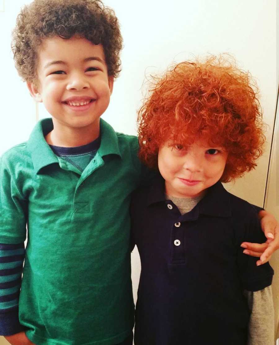 African American boy with red hair stands smiling arm in arm with his brother 