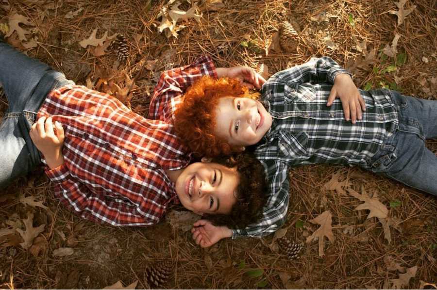 African American boy with red hair lays on back outside with head beside older brother