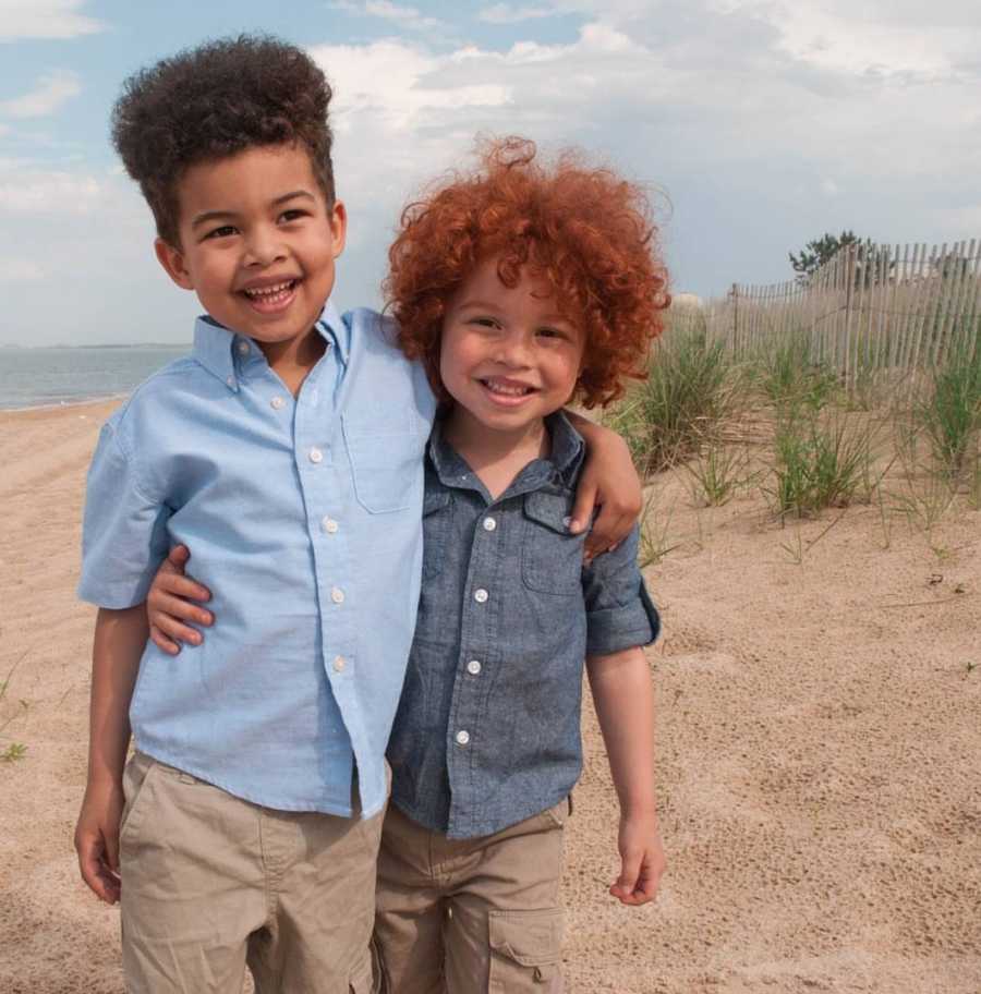 African American brothers, one of which who has red hair, stand smiling arm in arm on beach
