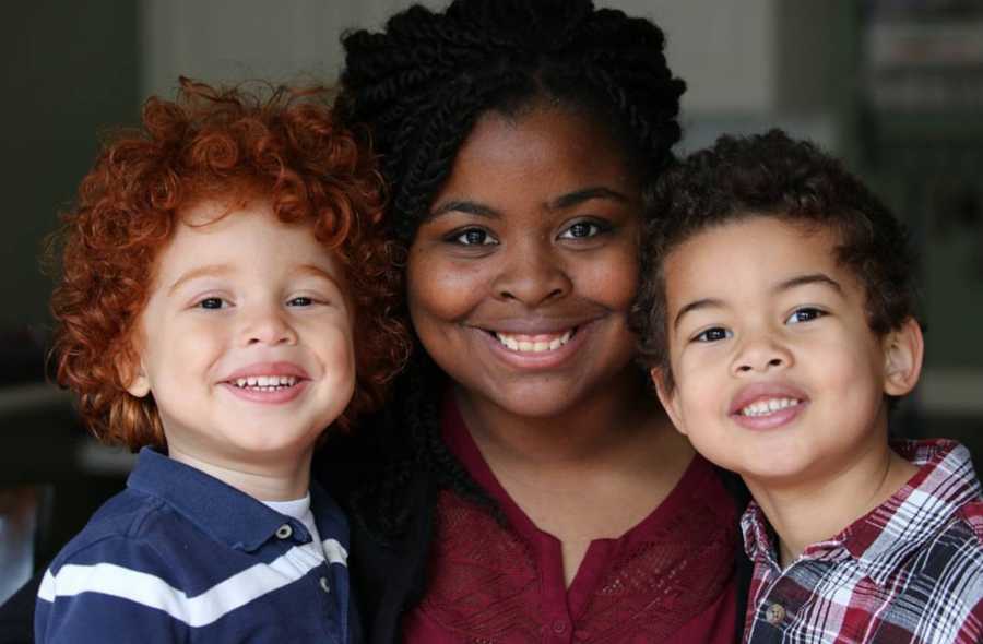 African American mother smiles with her two sons by her side, one of which has red curly hair