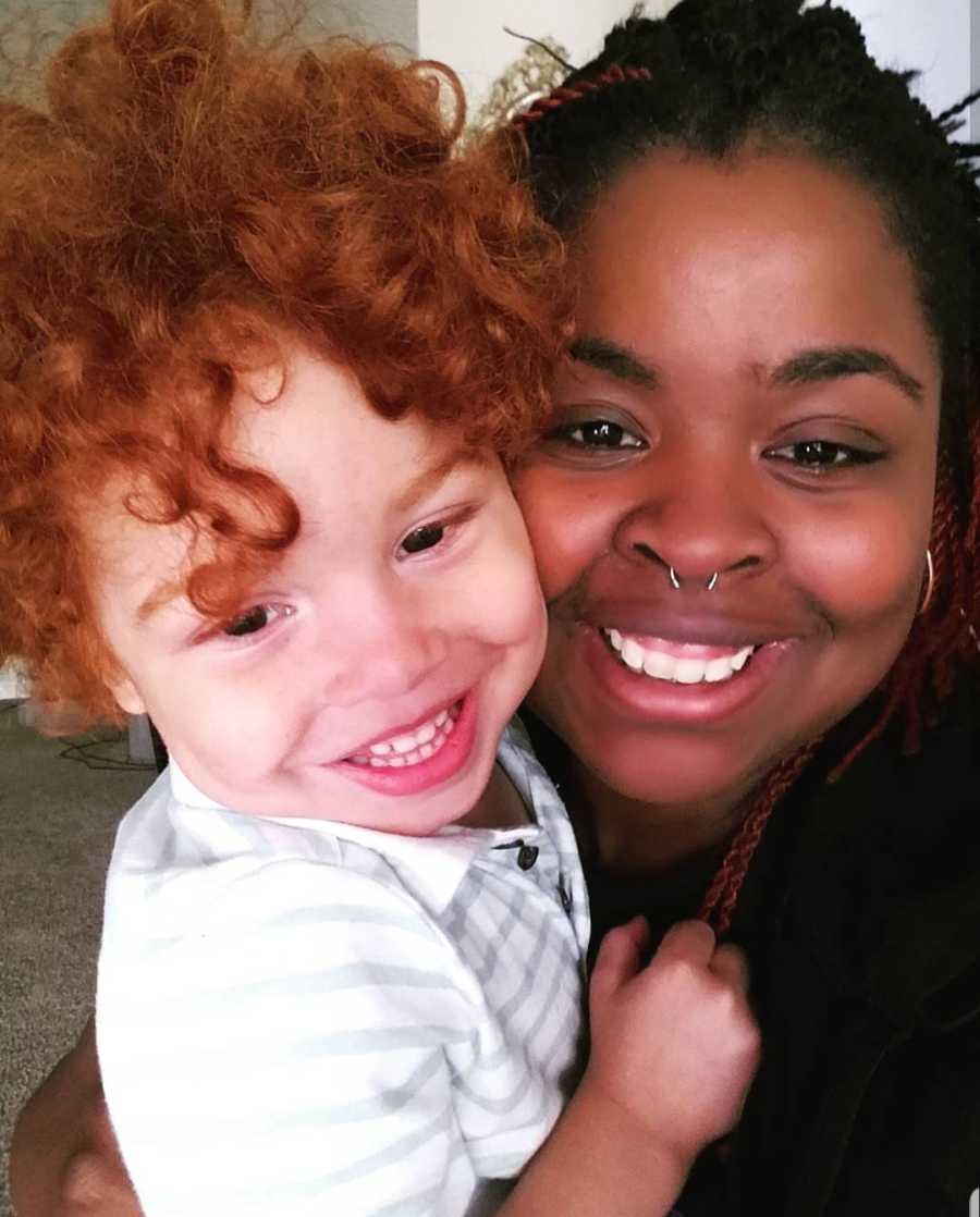 African American mother smiles in selfie with young son with red curly hair