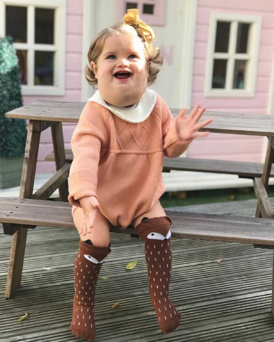 Little girl with cystic hygroma sits smiling at wooden picnic table