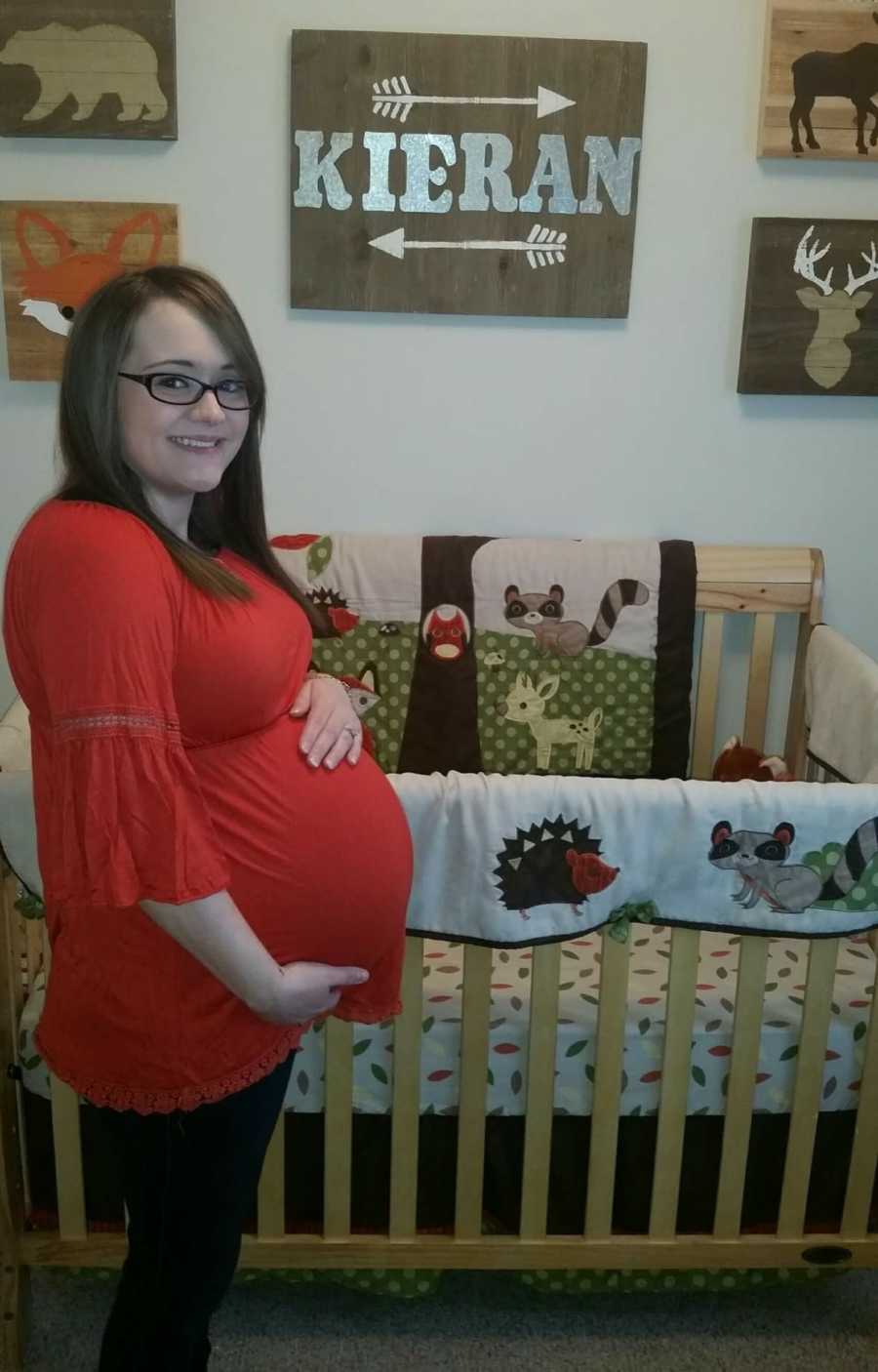 Pregnant woman with endometriosis stands beside crib for little boy