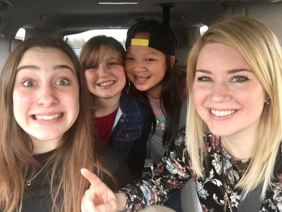 Mother smiles in car with biological daughter and two adopted daughters in selfie