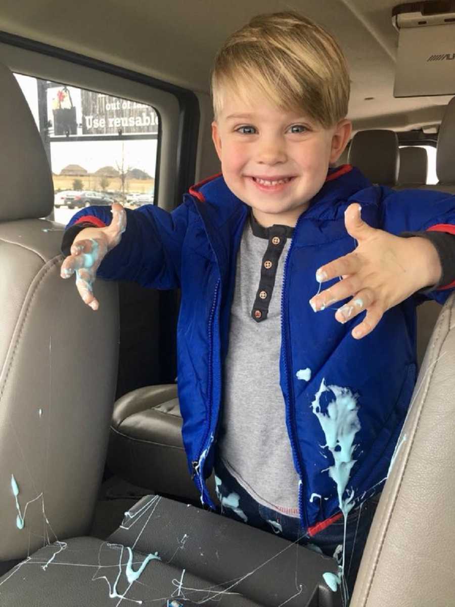 Little boy with nickname "Hurricane Ethan" stands in car smiling with blue goo all over himself and car