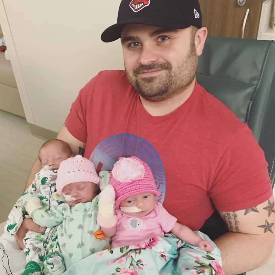 Father with Chiari Malformation sits in hospital holding triplets in his lap
