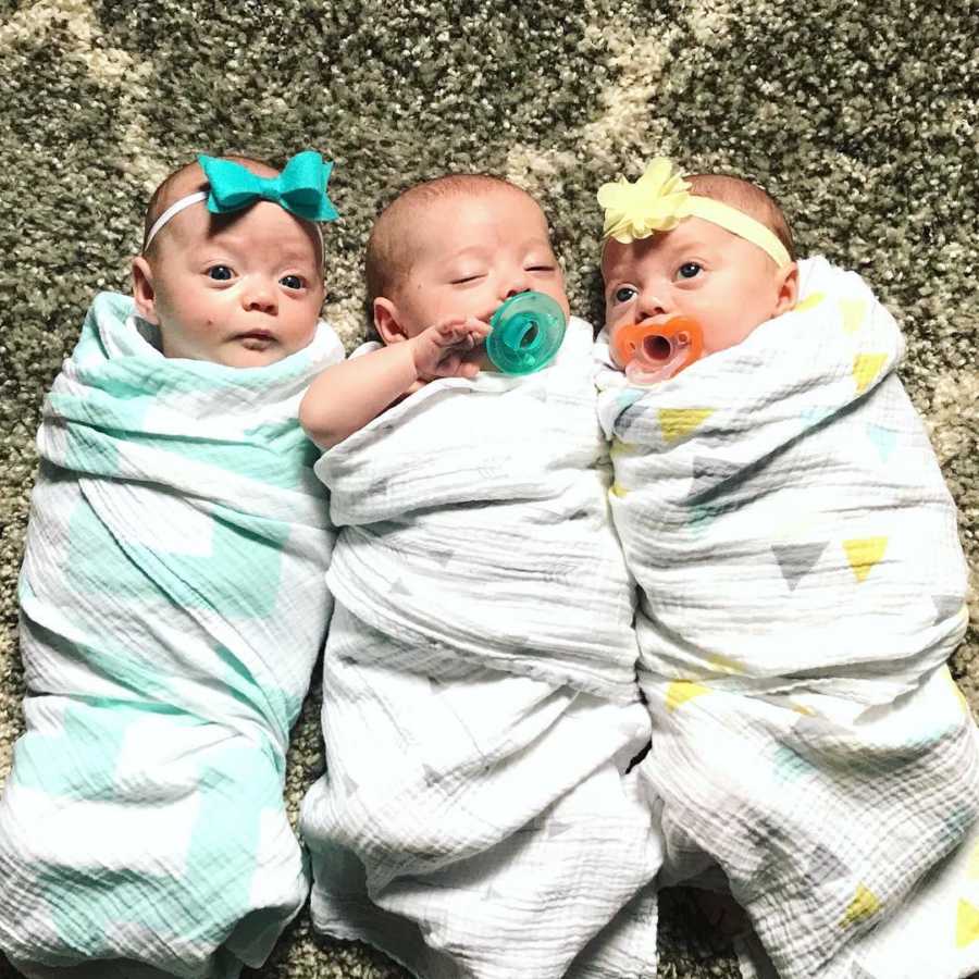 Triplets lay on their backs swaddled in blankets