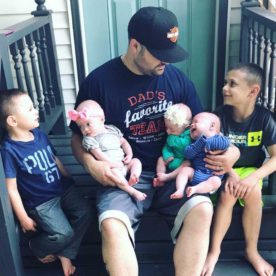 Dad with Chiari Malformation sits on steps outside of home with two older sons and baby triplets