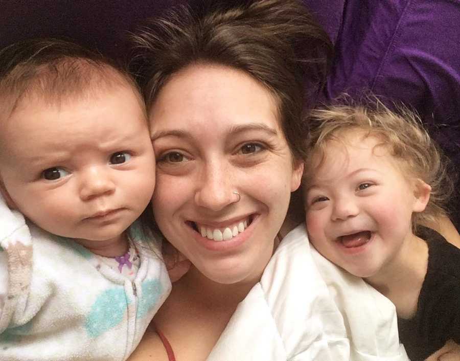 Mother smiles in selfie with newborn and daughter with down syndrome