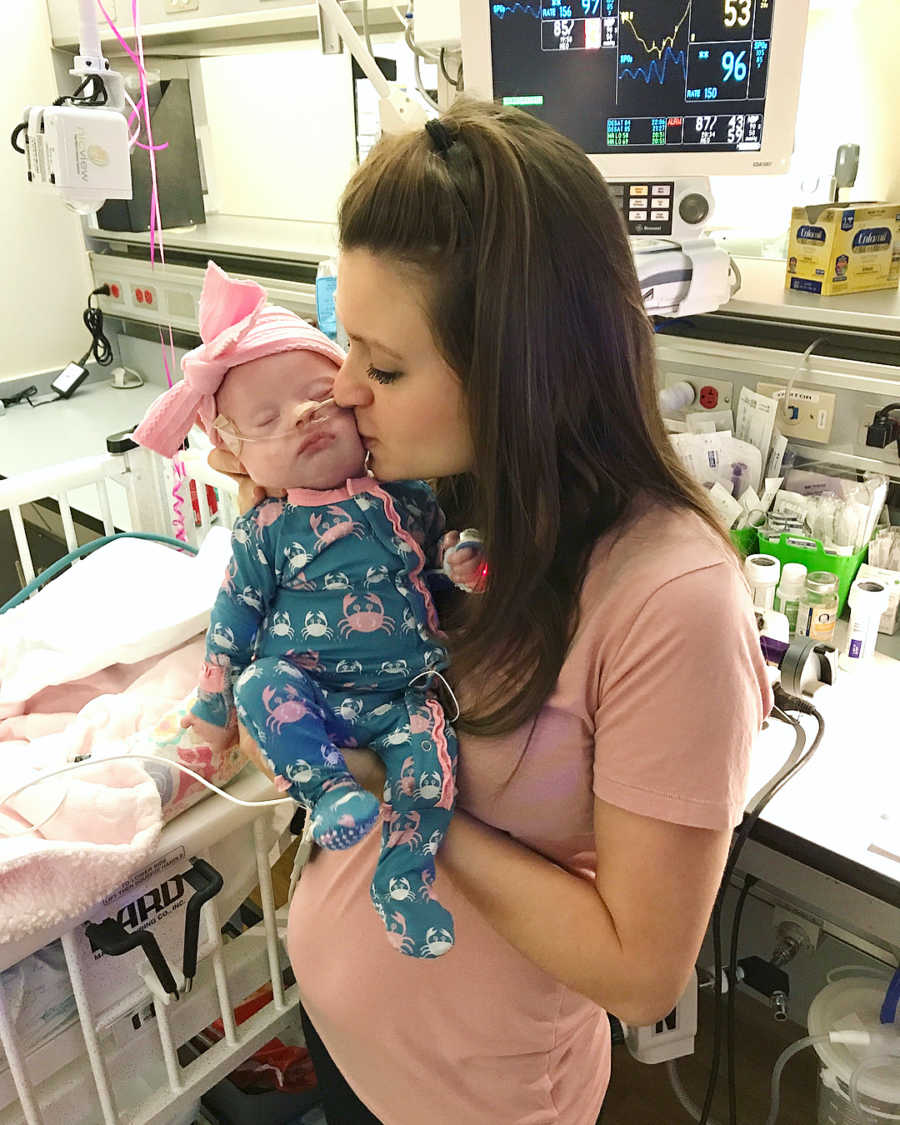 Mother stands in NICU kissing cheek of daughter who has down syndrome
