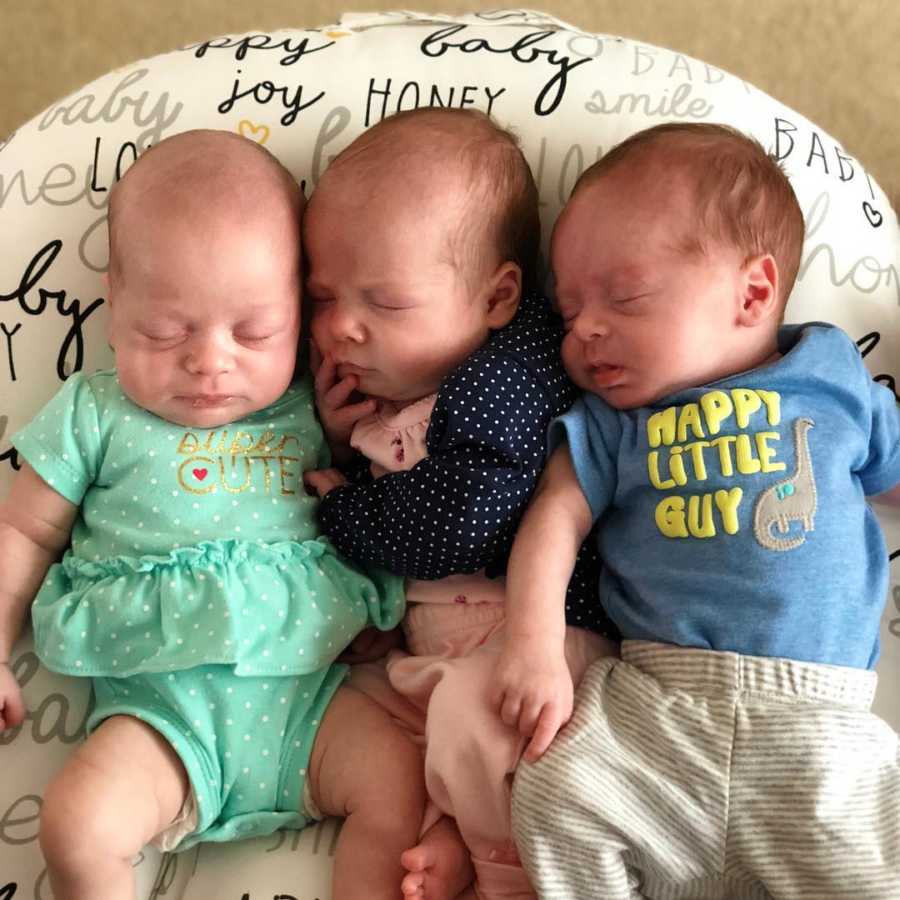 Newborn triplets lay asleep at home on pillow