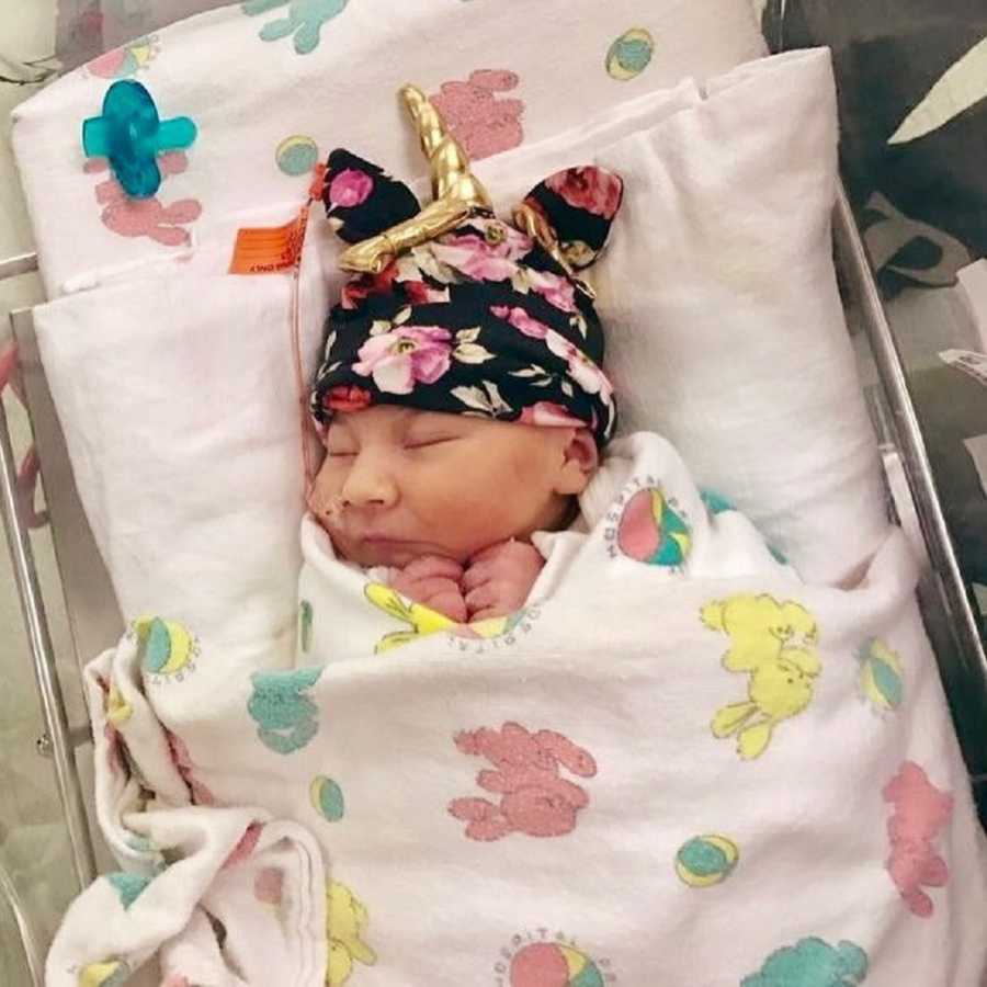 Newborn with Lissencephaly lays swaddled in NICU with unicorn hat on