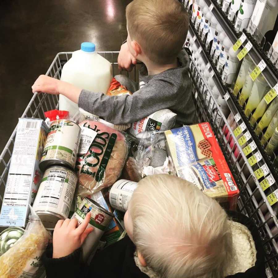 Two young children sit in shopping cart full of groceries