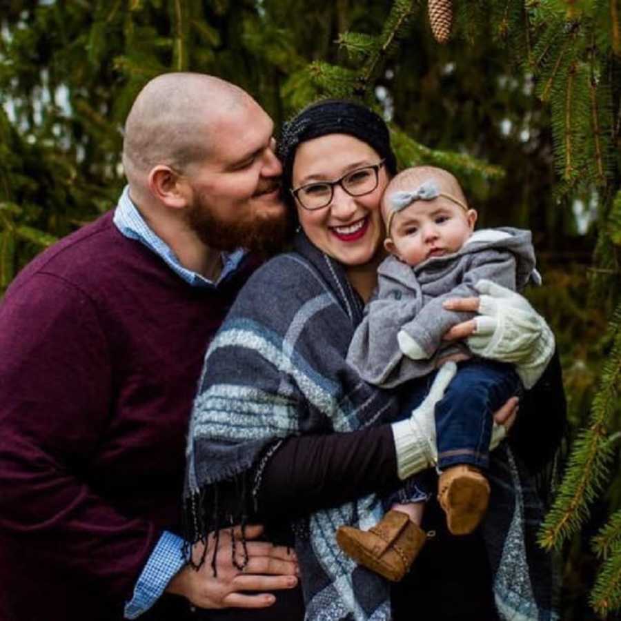 Man smiles beside girlfriend as she smiles holding their baby