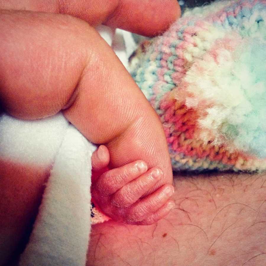 Close up of preemie baby's hand holding adult's finger