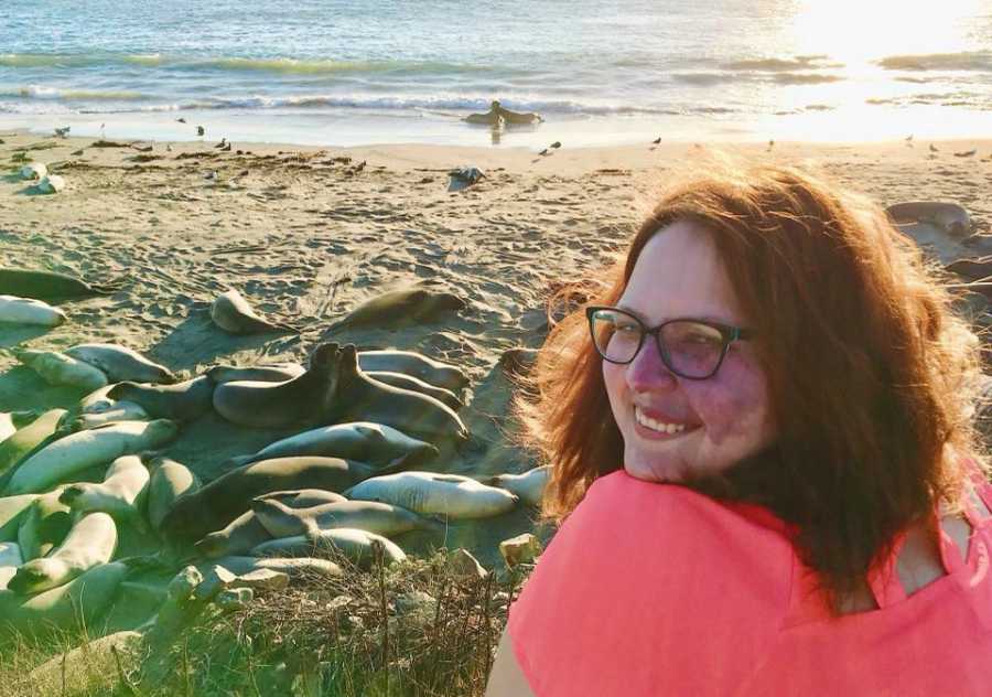 Woman who was fat shamed on plane sits beside beach filled with seals smiling over her shoulder