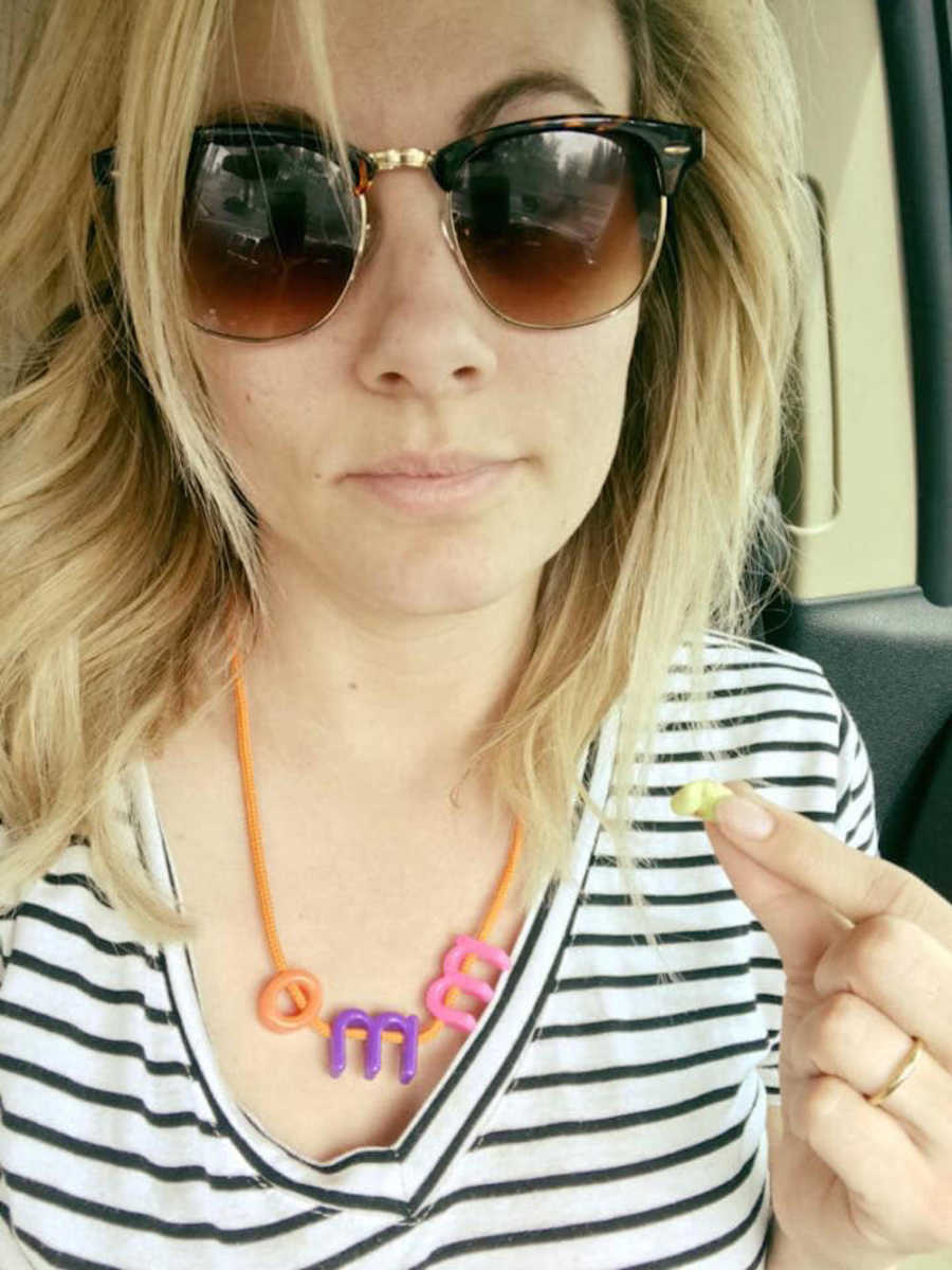 Mother with sunglasses on takes selfie in car as she wears necklace her child made for her