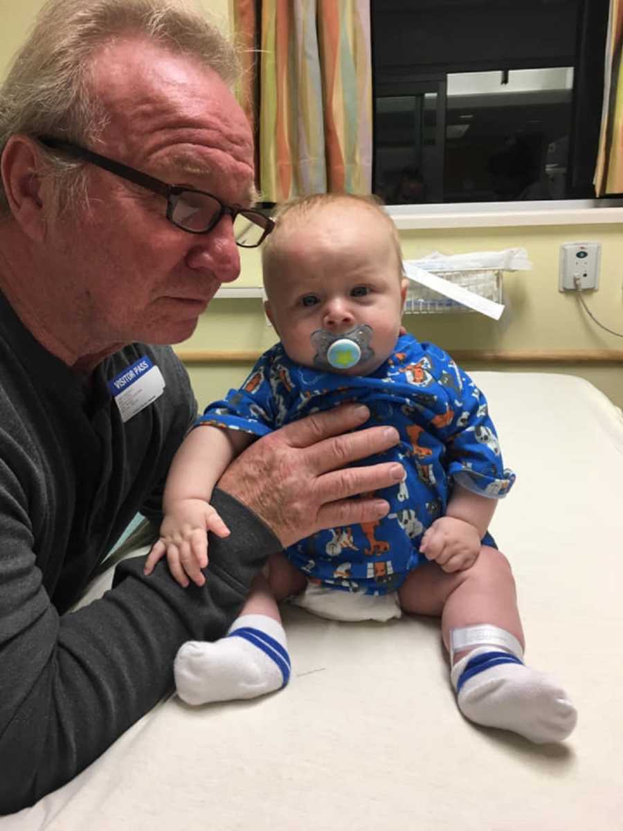 Grandfather holds baby with tumors in his stomach up on doctor's office