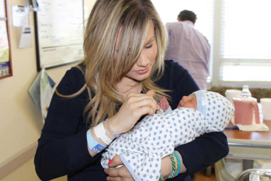 Mother stands in hospital room looking down at baby boy in her arms 