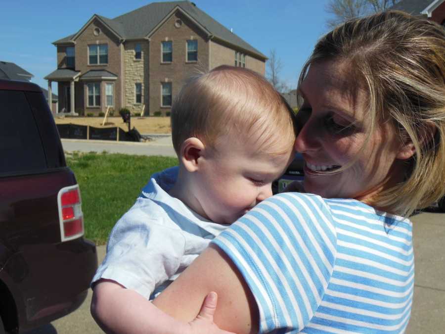 Woman smiles in driveway as she holds third child