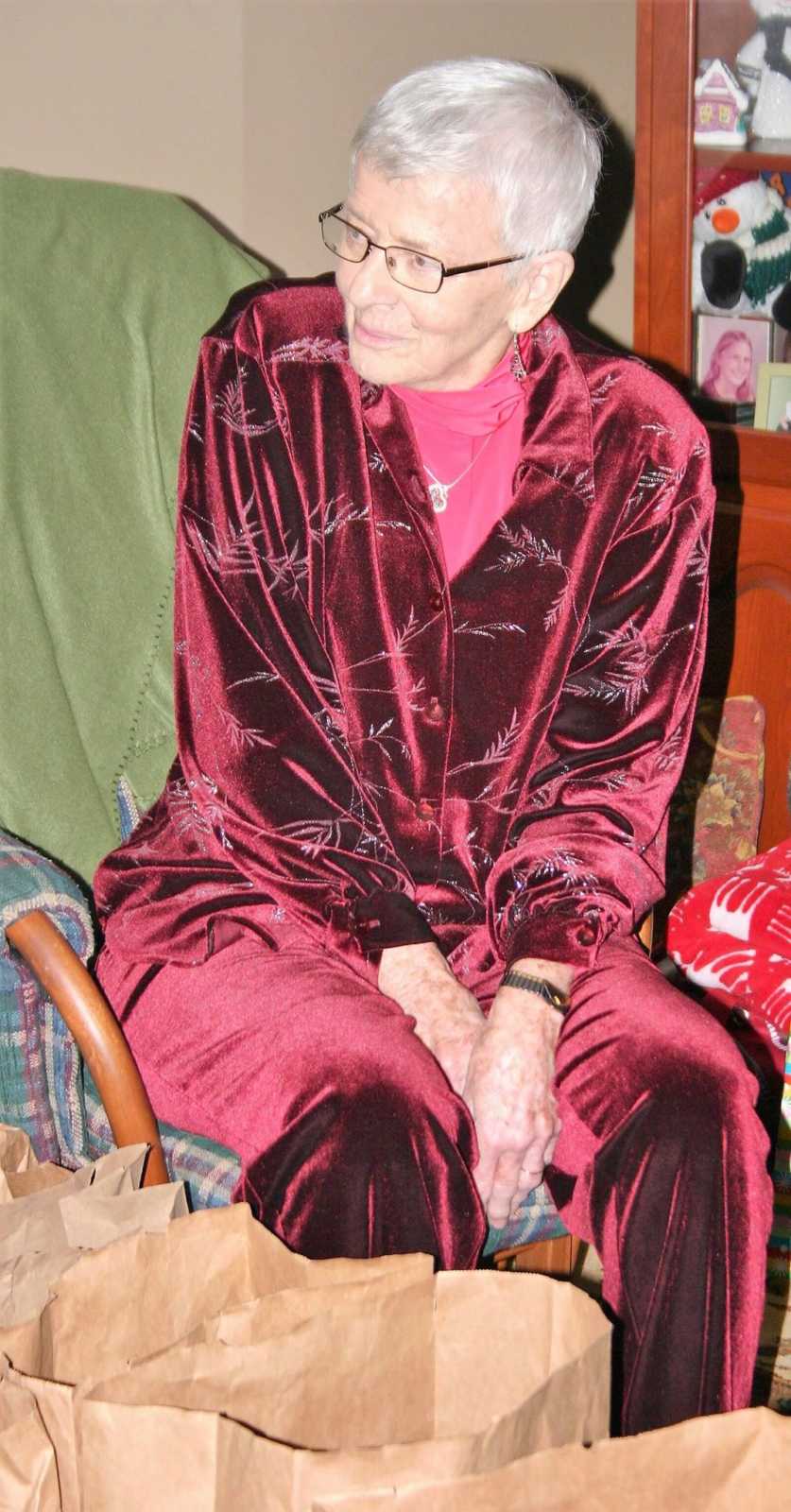 Elderly woman with dementia sits in chair at home wearing red velvet outfit for Christmas