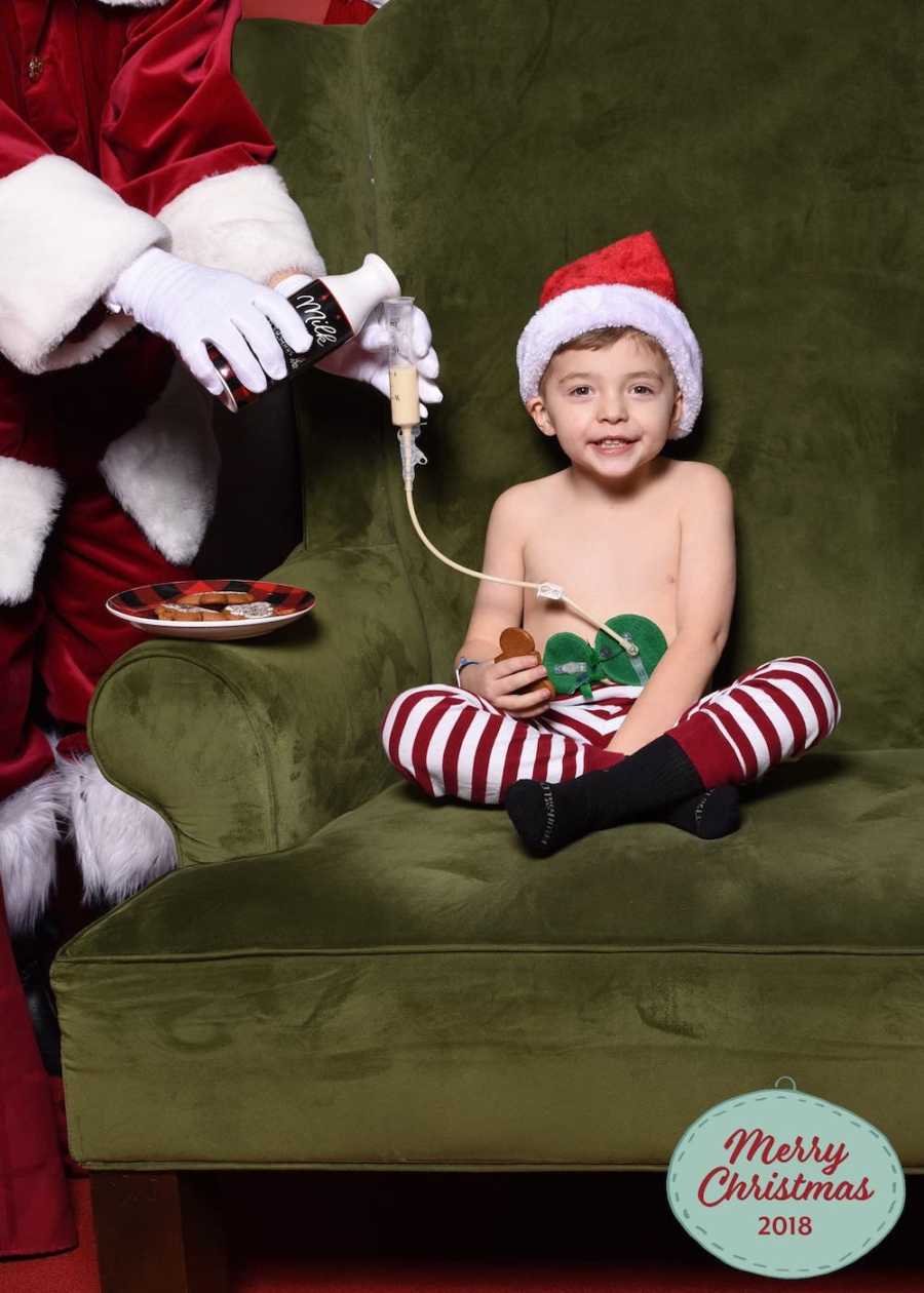 Little boy with stomach tube sits in green chair while Santa pours milk into his tube