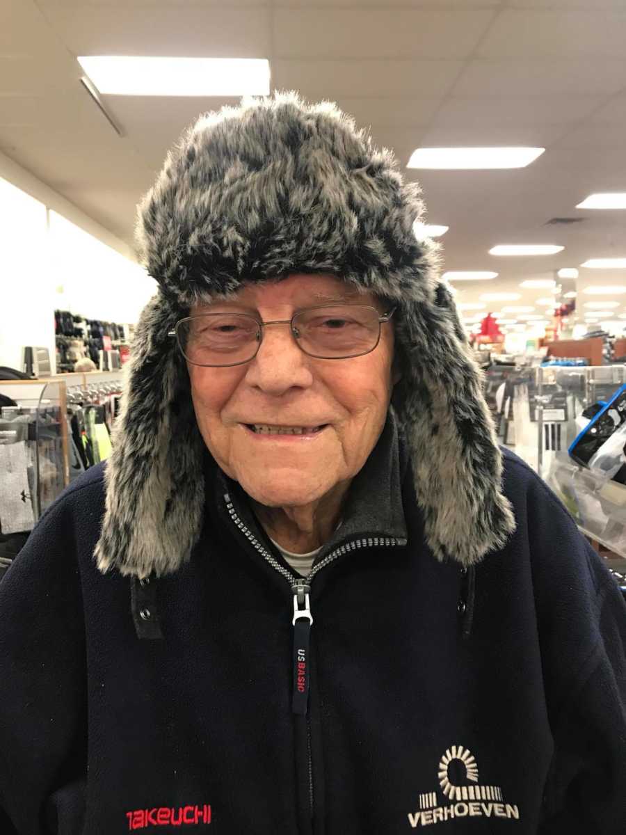 Elderly man smiles in store as he wears furry winter hat