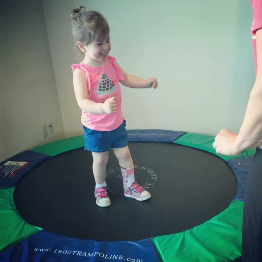 Little girl who had Hemorrhagic Stroke stands on mini trampoline with brace on her ankle
