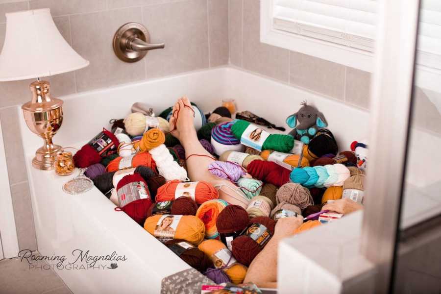 Woman laying in bathtub full of bundles of yarn