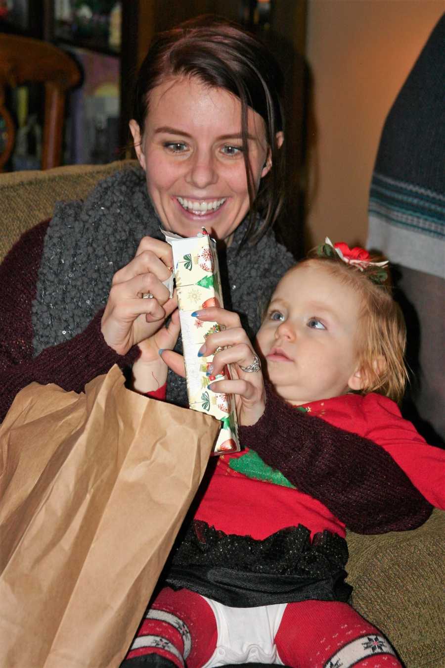 Woman smiles while sitting with baby on her lap as she opens present